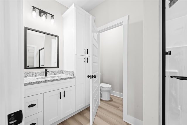 full bath with baseboards, vanity, toilet, and wood finished floors