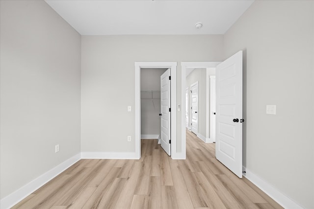 unfurnished bedroom featuring a closet, baseboards, a spacious closet, and light wood finished floors