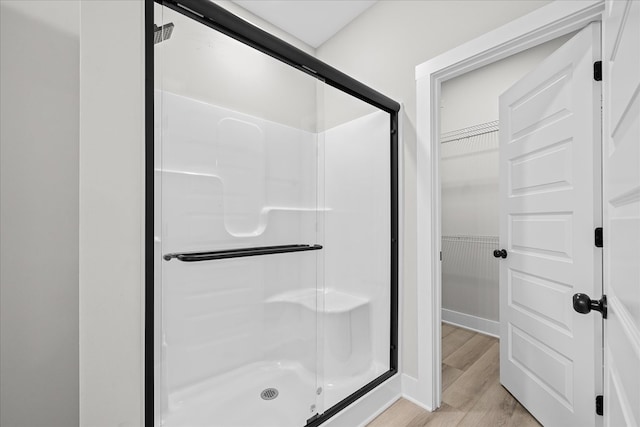 bathroom with a spacious closet, a stall shower, and wood finished floors