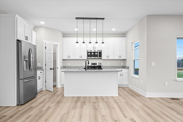 kitchen featuring stainless steel appliances, decorative light fixtures, an island with sink, and white cabinetry