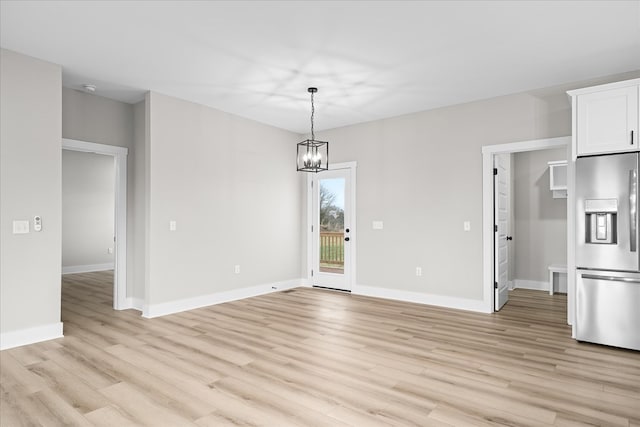 unfurnished dining area with light wood-style flooring, baseboards, and a notable chandelier