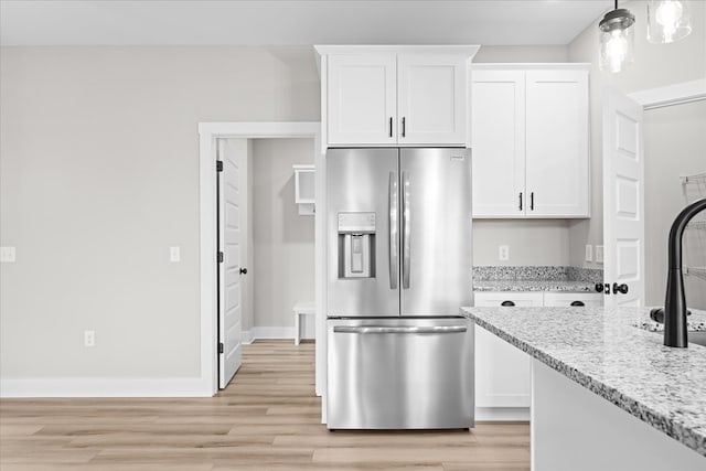 kitchen with light stone counters, hanging light fixtures, light wood-style floors, white cabinets, and stainless steel fridge