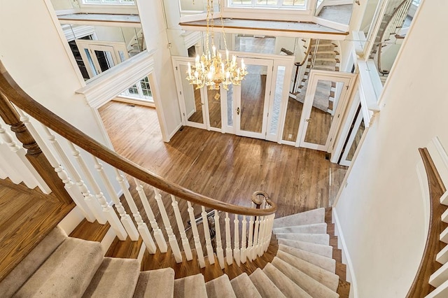 stairs with a chandelier, wood finished floors, and a healthy amount of sunlight