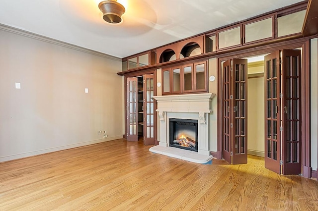 unfurnished living room with a lit fireplace, ornamental molding, light wood-style flooring, and baseboards