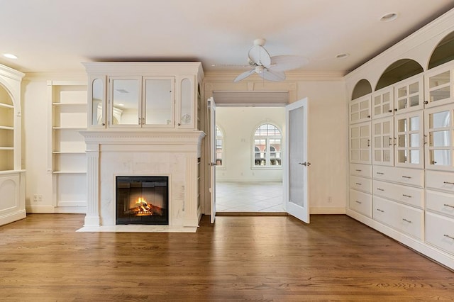 unfurnished living room featuring wood finished floors, a high end fireplace, baseboards, a ceiling fan, and ornamental molding