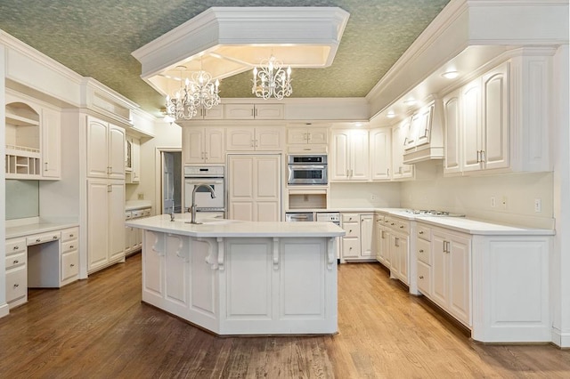 kitchen with decorative light fixtures, light countertops, light wood-type flooring, a center island with sink, and an inviting chandelier