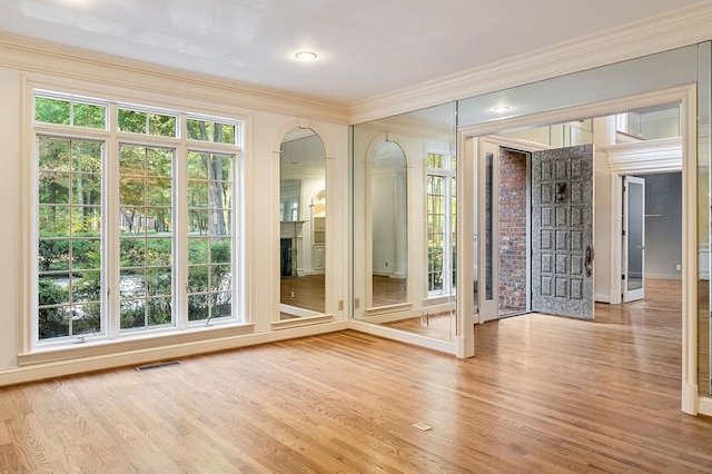 interior space with crown molding, arched walkways, visible vents, and light wood-style floors