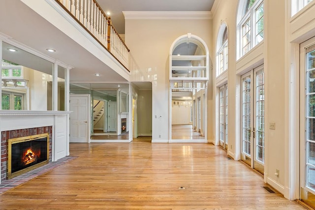 entrance foyer with light wood-style flooring, a high ceiling, visible vents, a glass covered fireplace, and crown molding