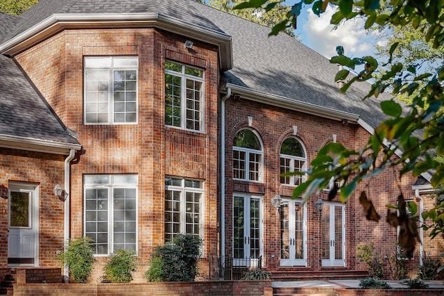 view of home's exterior featuring roof with shingles, french doors, and brick siding