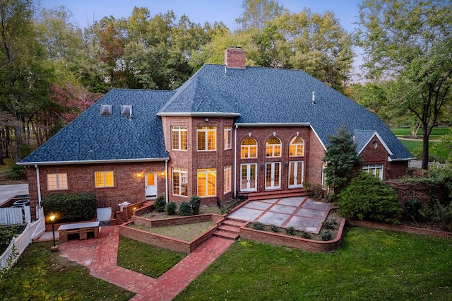 rear view of house with a patio area, roof with shingles, brick siding, and a yard