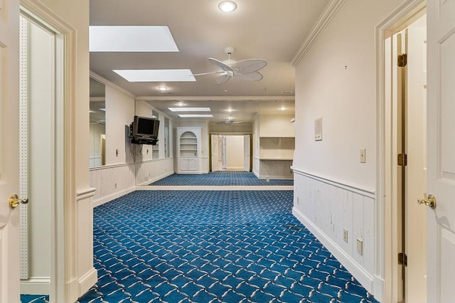 hall featuring carpet floors, a skylight, ornamental molding, and a wainscoted wall