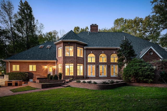 rear view of property with a shingled roof, a chimney, a lawn, and brick siding