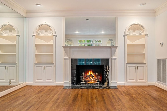 unfurnished living room featuring built in features, visible vents, a premium fireplace, ornamental molding, and wood finished floors