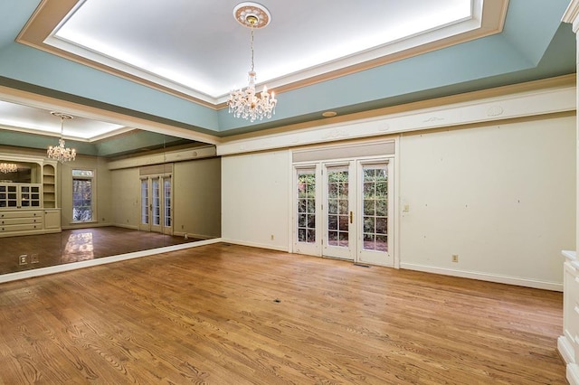 unfurnished living room with a chandelier, a tray ceiling, crown molding, and wood finished floors