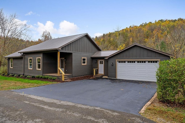 view of front facade with aphalt driveway, a forest view, metal roof, and an attached garage