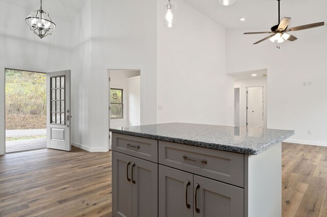 kitchen with light stone counters, hanging light fixtures, gray cabinetry, a kitchen island, and wood finished floors