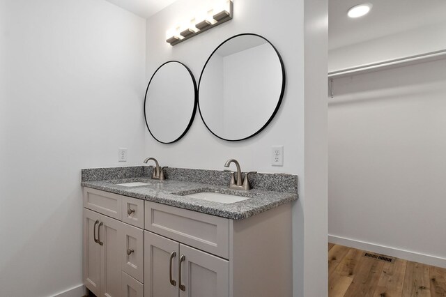 bathroom with double vanity, wood finished floors, a sink, and baseboards