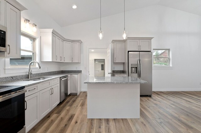 kitchen with light stone counters, a sink, a kitchen island, hanging light fixtures, and appliances with stainless steel finishes