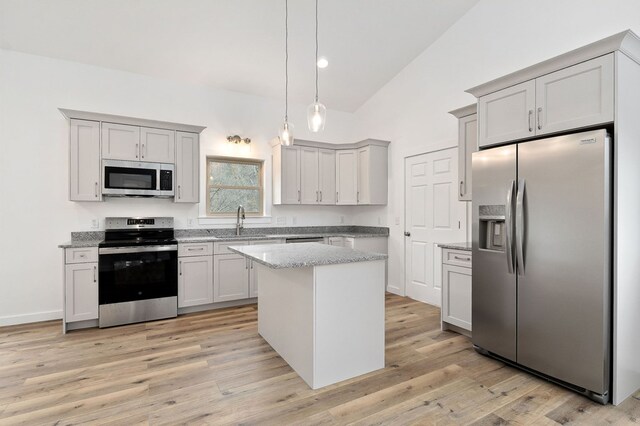 kitchen with a kitchen island, appliances with stainless steel finishes, decorative light fixtures, vaulted ceiling, and a sink