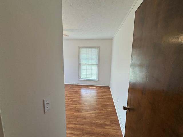 hallway featuring a textured ceiling, crown molding, baseboards, and wood finished floors