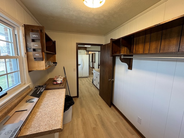 kitchen with light countertops, ornamental molding, light wood-style flooring, white fridge with ice dispenser, and a textured ceiling