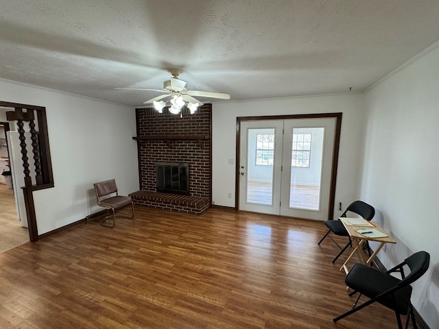 unfurnished living room with wood finished floors, ornamental molding, ceiling fan, a textured ceiling, and a brick fireplace