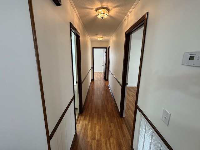 corridor featuring a textured ceiling, crown molding, and dark wood-style flooring