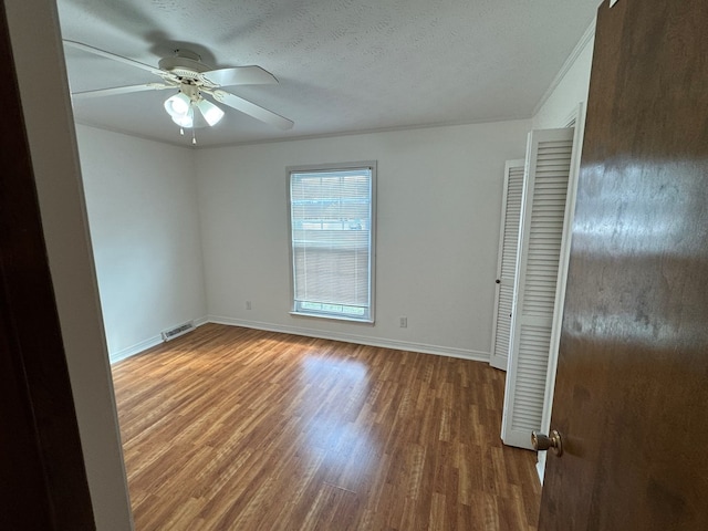 empty room with visible vents, baseboards, wood finished floors, a textured ceiling, and a ceiling fan