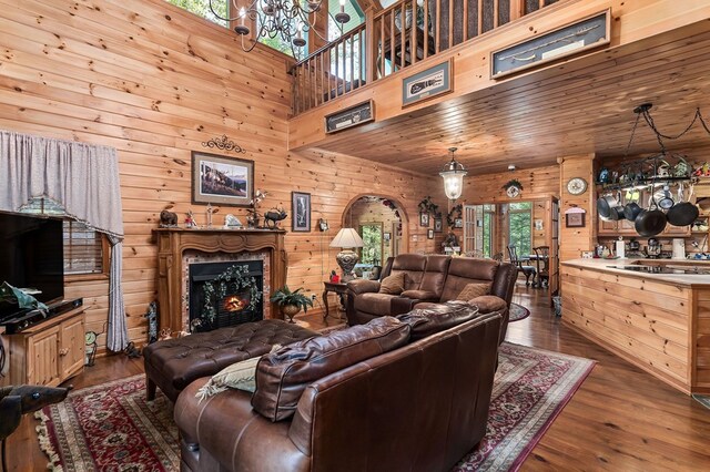 living area with a high ceiling, dark wood-type flooring, wood ceiling, wooden walls, and a warm lit fireplace