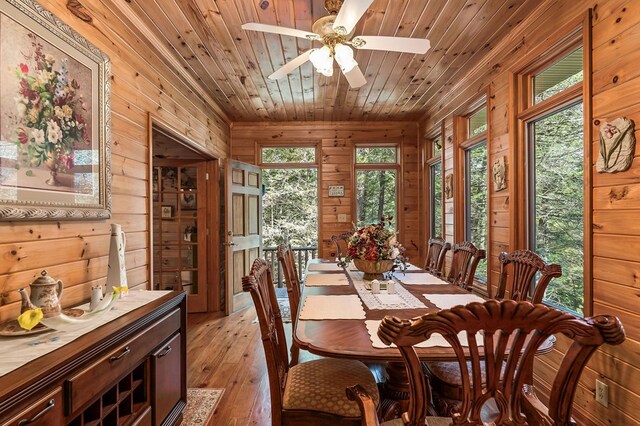 dining area with ceiling fan, light wood-type flooring, wood walls, and wooden ceiling