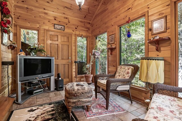 interior space with a wealth of natural light, lofted ceiling, stone tile flooring, and wooden walls