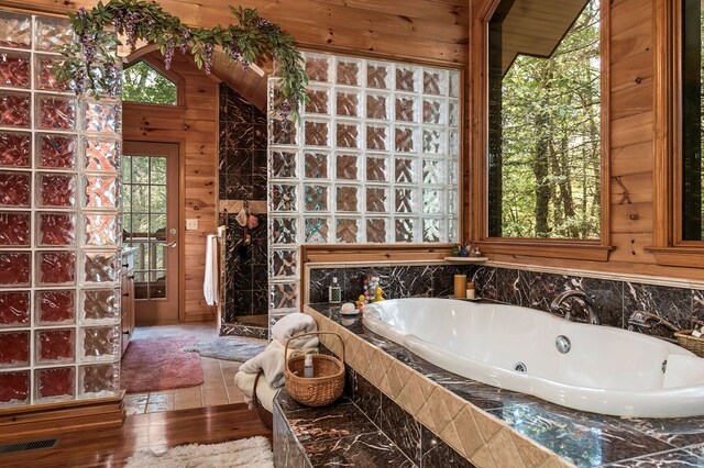 full bathroom featuring a bath, wood finished floors, visible vents, and wooden walls