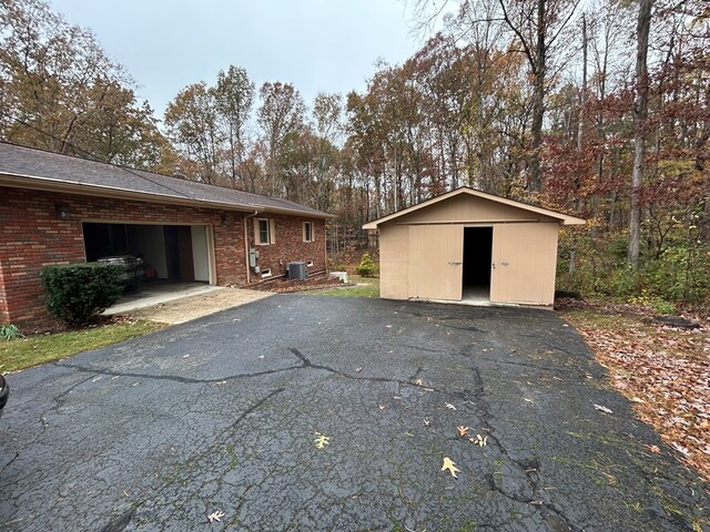 exterior space with aphalt driveway, an attached garage, brick siding, and central air condition unit