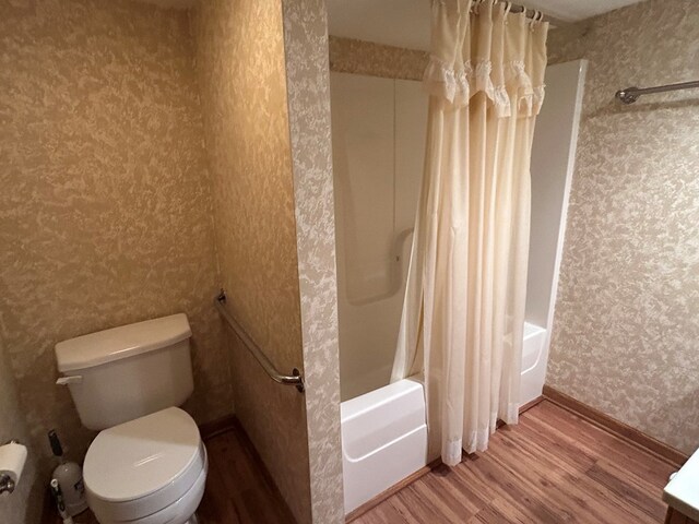 bathroom with wallpapered walls, wood finished floors, toilet, and shower / bathtub combination with curtain