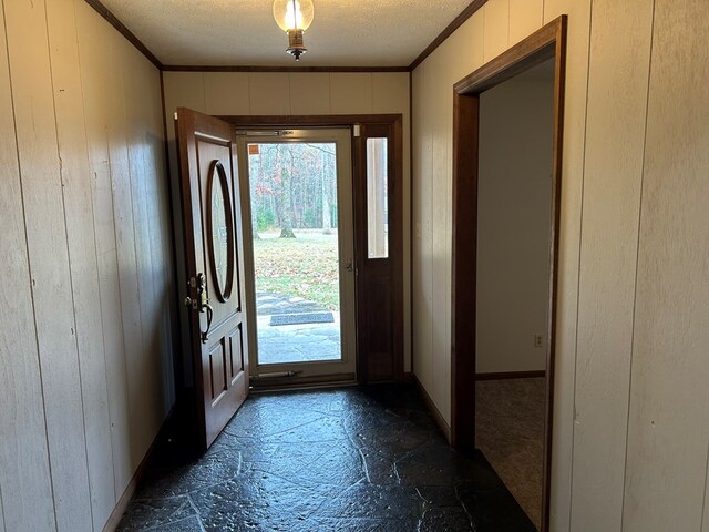 doorway with wooden walls, a textured ceiling, and crown molding