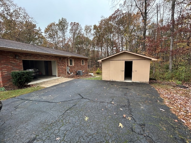 exterior space with central air condition unit, a garage, aphalt driveway, and brick siding