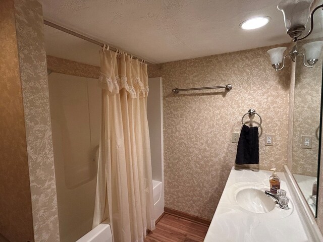 bathroom featuring shower / bathtub combination with curtain, vanity, a textured ceiling, wood finished floors, and wallpapered walls