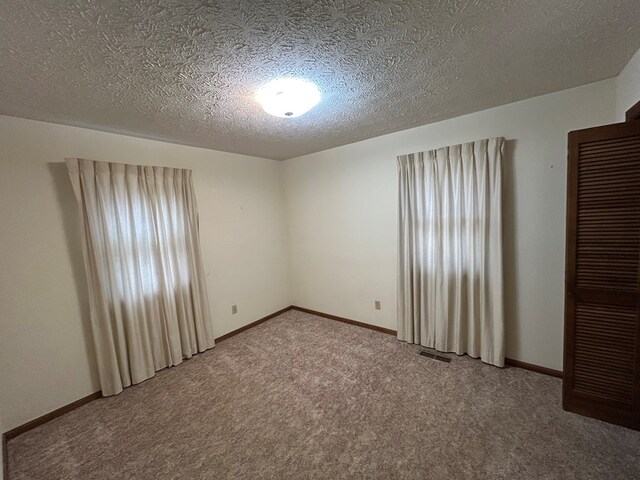 spare room featuring a textured ceiling, carpet flooring, visible vents, and baseboards