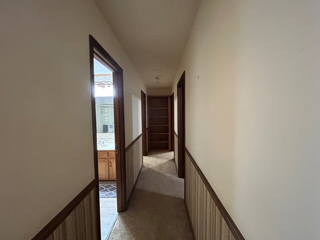 hallway featuring wainscoting, a sink, and light colored carpet