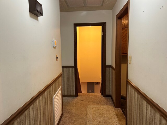 corridor featuring a wainscoted wall and light carpet