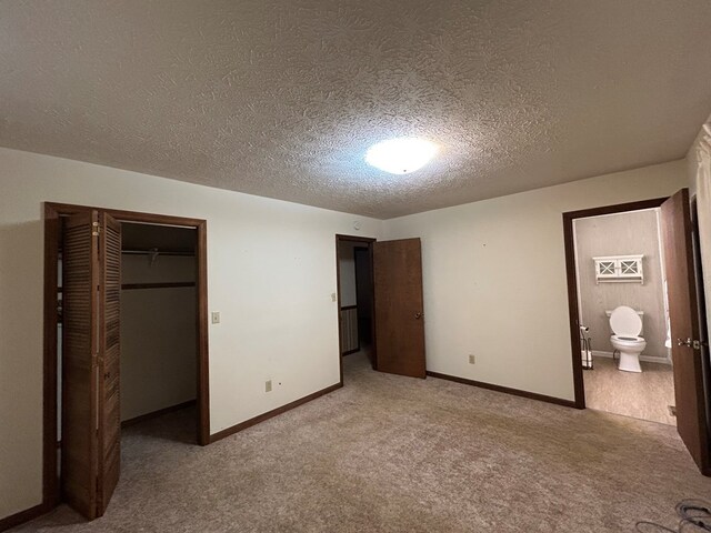 unfurnished bedroom featuring a closet, light carpet, connected bathroom, a textured ceiling, and baseboards