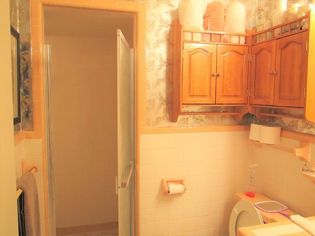 full bathroom featuring a wainscoted wall, a shower stall, tile walls, and wallpapered walls