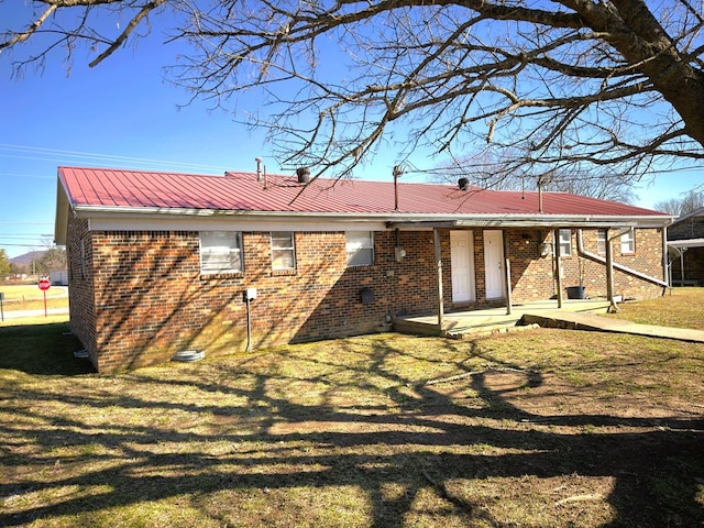 back of property with a yard, metal roof, and brick siding