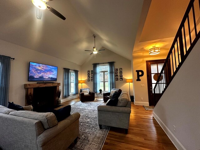 living area featuring ceiling fan, wood finished floors, baseboards, vaulted ceiling, and stairway