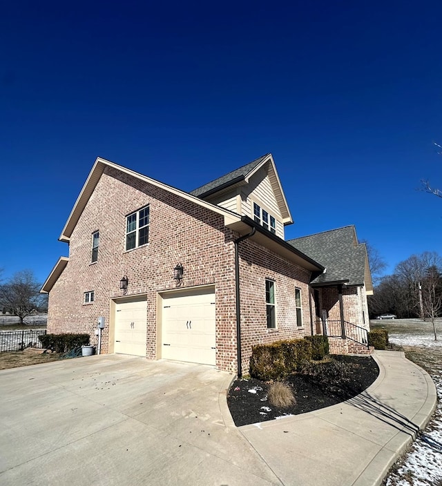 view of side of home with driveway, brick siding, and fence