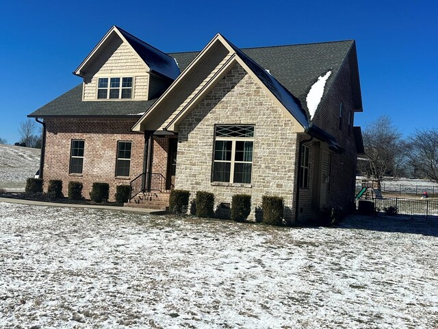 view of front of home featuring stone siding, fence, and brick siding