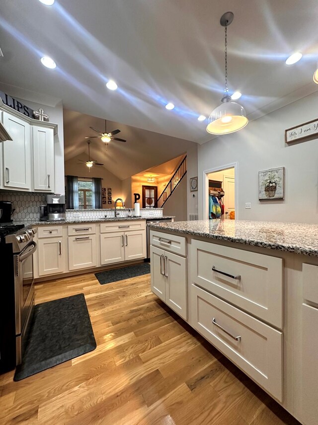 kitchen with light stone counters, a sink, white cabinetry, light wood finished floors, and stainless steel range with gas stovetop