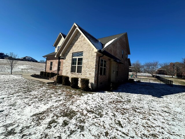 view of snowy exterior featuring stone siding, brick siding, and fence