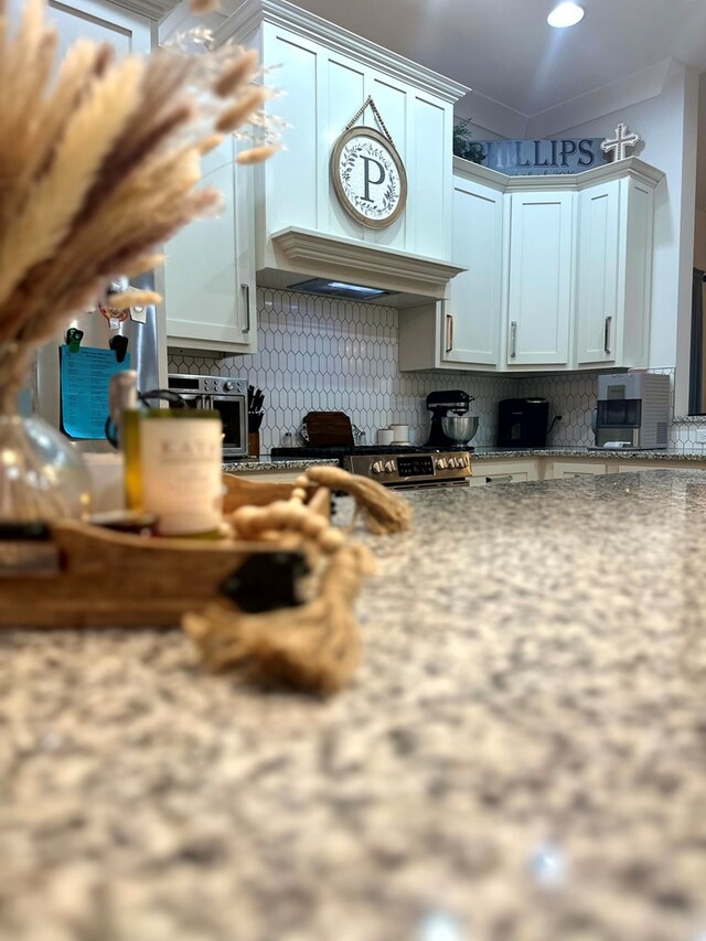 kitchen featuring tasteful backsplash, white cabinetry, custom range hood, and light stone countertops