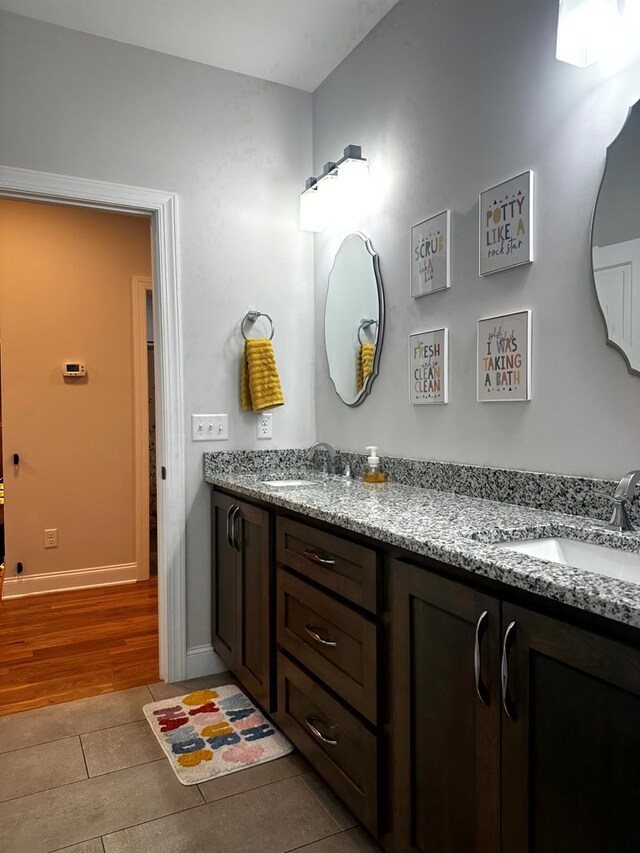 bathroom featuring double vanity, baseboards, a sink, and wood finished floors